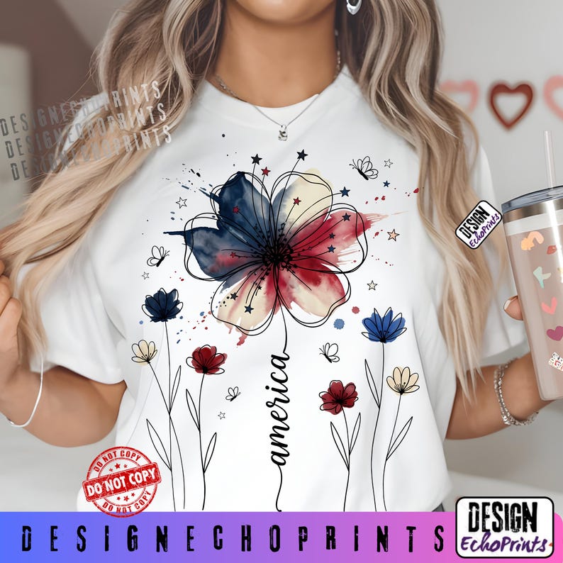 K&ouml;nnte beinhalten: Wei&szlig;es T-Shirt mit einem Aquarell-Blumendesign in Rot, Wei&szlig; und Blau, mit dem Wort "america" in Schreibschrift. Das Design umfasst Schmetterlinge und Sterne. Das Shirt hat einen Rundhalsausschnitt und kurze &Auml;rmel.