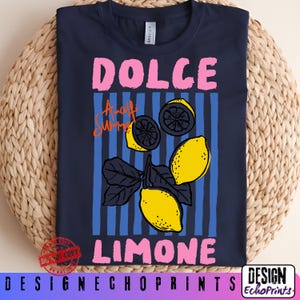 Puede incluir: Camiseta azul marino con un dise&ntilde;o gr&aacute;fico. El dise&ntilde;o presenta las palabras "DOLCE LIMONE" en rosa y "Amalfi Summer" en naranja. El dise&ntilde;o incluye limones amarillos y rayas verticales azules. La camiseta se muestra sobre una superficie tejida.