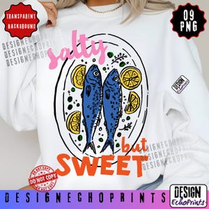 Puede incluir: Sudadera blanca con un gr&aacute;fico de dos peces azules en un plato con rodajas de lim&oacute;n. El texto "salty but sweet" est&aacute; en rosa y naranja. El dise&ntilde;o incluye el texto "Design EchoPrints".