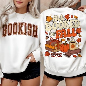 Puede incluir: Sudadera blanca con la palabra "BOOKISH" en letras marrones en la parte delantera. La parte trasera presenta un gr&aacute;fico con tem&aacute;tica oto&ntilde;al con el texto "ALL BOOKED for FALL", calabazas, libros y hojas.