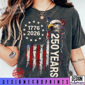 Puede incluir: Camiseta gris oscuro con un dise&ntilde;o de la bandera estadounidense, el texto "1776 2026" y "250 YEARS". El dise&ntilde;o incluye una cabeza de &aacute;guila y rayos. La camiseta tiene un aspecto desgastado.