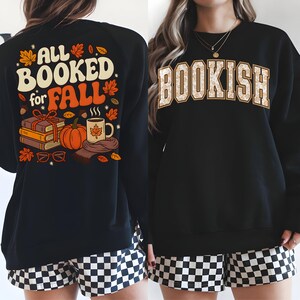 Puede incluir: Sudadera negra con un gr&aacute;fico de "ALL BOOKED for FALL" en la espalda, con libros, una calabaza y una taza. La parte delantera muestra "BOOKISH" en una fuente universitaria. La sudadera se combina con pantalones cortos a cuadros blancos y negros.