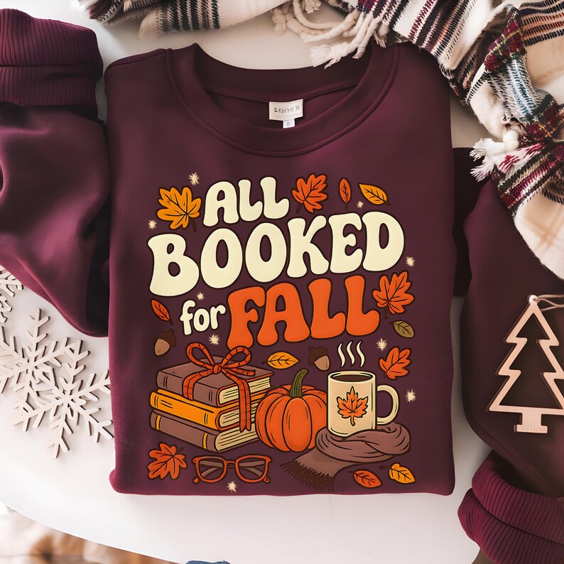 Puede incluir: Sudadera burdeos con el texto "ALL BOOKED for FALL" en naranja y blanco. El dise&ntilde;o incluye ilustraciones oto&ntilde;ales de hojas, una calabaza, libros, una taza y gafas. Un gr&aacute;fico con tem&aacute;tica oto&ntilde;al.