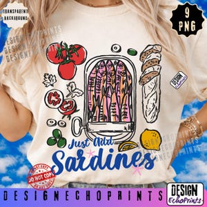 Puede incluir: Camiseta color crema con un dise&ntilde;o de sardinas colorido. El gr&aacute;fico incluye una lata de sardinas, tomates, aceitunas, pan y el texto "Just Add Sardines". Tambi&eacute;n se ve una rodaja de lim&oacute;n y las palabras "Design EchoPrints".