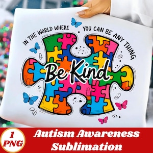 Puede incluir: Una almohada blanca con un diseño de rompecabezas colorido y las palabras "Be Kind". El diseño incluye mariposas y el texto "In the world where you can be anything". La parte inferior de la almohada tiene el texto "Autism Awareness Sublimation".
