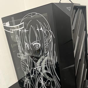 May include: Black computer tower with a tempered glass side panel featuring a white anime character design. The words "GEFORCE RTX" are visible. The tower has a sleek, modern design with angled edges and a mesh front panel.