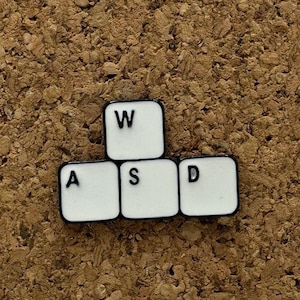 Könnte beinhalten: Weiße Kunststoff-Tastaturtasten mit den Buchstaben W, A, S und D auf einem Korkuntergrund.