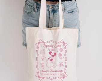 May include: Cream tote bag with a pink graphic. The graphic includes the text "Happily Ever After" and "Ashley's Bachelorette DISNEY WORLD FL". The design features Minnie Mouse and other themed illustrations.