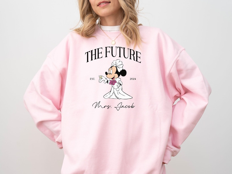 May include: Pink sweatshirt with a graphic of a cartoon bride Mickey Mouse with the text "The Future Est. 2024 Mrs. Jacob"
