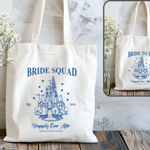 May include: Two white canvas tote bags with blue text and a blue illustration of Cinderella's castle. The bag on the left says "Bride Squad" and the bag on the right says "Bride to Be". Both bags say "Happily Ever After" and "Magic Kingdom, Florida".