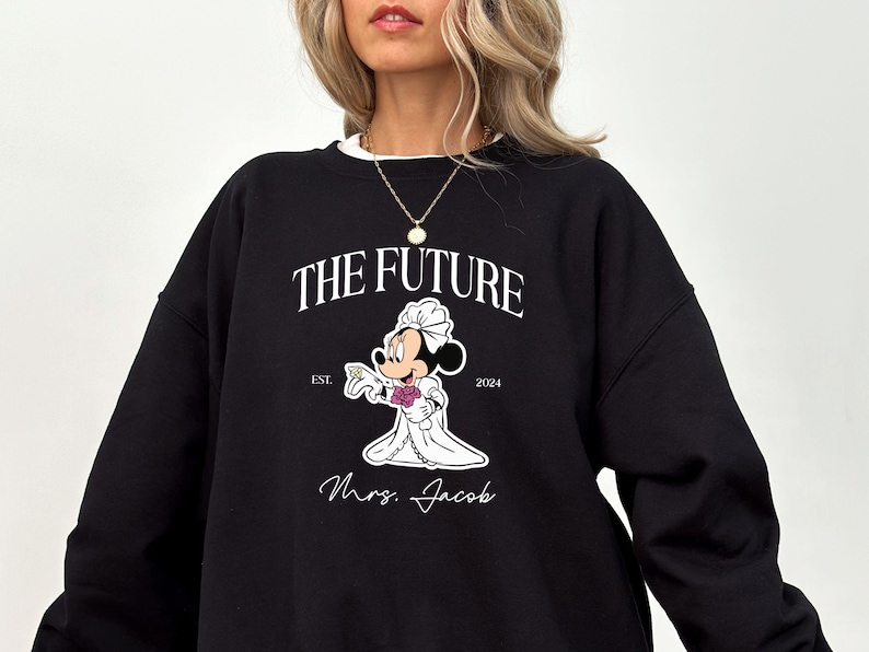 May include: Black sweatshirt with a white graphic of Mickey Mouse dressed as a bride. The text "The Future" is above Mickey Mouse and "Est. 2024" is below. The text "Mrs. Jacob" is below Mickey Mouse.
