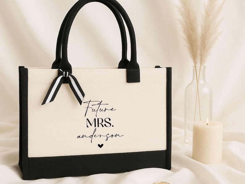 Op de afbeelding: Een witte canvas tote bag met zwarte afwerking en handvatten. De tas heeft een zwarte strik en de tekst "Future Mrs. Anderson" gedrukt op de voorkant.