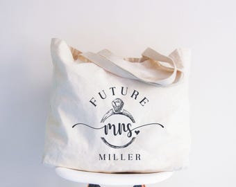 May include: White canvas tote bag with black text that reads "Future Mrs. Miller" and a drawing of a ring with a diamond.
