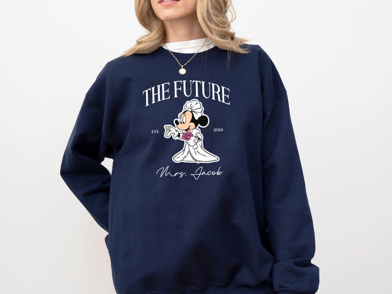 May include: A navy blue sweatshirt with a white graphic of Mickey Mouse dressed as a bride. The graphic includes the text "The Future" with the years "Est. 2024" and the text "Mrs. Jacob".