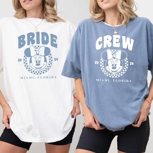 Puede incluir: Dos camisetas blancas con un gr&aacute;fico azul de Minnie Mouse, la novia de Mickey Mouse, con el texto "BRIDE" y "CREW" en la parte delantera. Las camisetas tambi&eacute;n tienen el texto "20 MIAMI, FLORIDA 24" en la parte delantera. Una camiseta es blanca y la otra es azul.