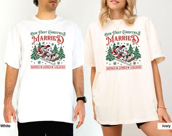 May include: A couple's matching white and ivory t-shirts with a Christmas-themed design featuring Mickey and Minnie Mouse riding a sleigh. The text on the shirts reads "Our First Christmas Married" with the couple's names and wedding date.