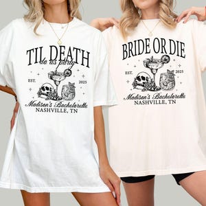 Peut inclure: Deux t-shirts blancs avec du texte et des graphismes noirs. Le premier t-shirt dit "Til Death do us party" avec un cr&acirc;ne et des os crois&eacute;s et deux verres &agrave; cocktail. Le deuxi&egrave;me t-shirt dit "Bride or Die" avec un cr&acirc;ne et des os crois&eacute;s et deux verres &agrave; cocktail. Les deux t-shirts disent "Madison's Bachelorette Nashville, TN" et "Est. 2025".