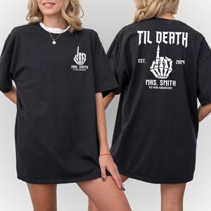 Może przedstawiać: Czarny T-shirt z białą szkieletową ręką pokazującą środkowy palec i tekstem "TIL DEATH" nad nią. Tekst "EST. 2024" znajduje się pod ręką, a tekst "MRS. SMITH VI-VIII-MMXXIV" pod nim.