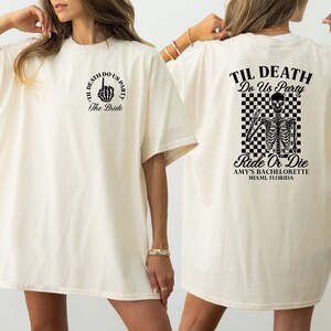 Może przedstawiać: Kremowa koszulka z czarnym tekstem graficznym i ilustracjami. Prz&oacute;d przedstawia gest dłoni i słowa "TIL DEATH DO US PARTY" i "The Bride". Tył przedstawia szkielet, kratkowane tło i słowa "Ride Or Die".