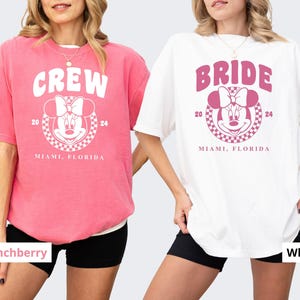 Puede incluir: Dos camisetas rosa y blancas con un gr&aacute;fico de un rat&oacute;n de dibujos animados con un lazo. La camiseta rosa dice "CREW" y la camiseta blanca dice "BRIDE". Ambas camisetas dicen "2024 MIAMI, FLORIDA".