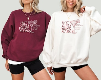 May include: Two white and maroon sweatshirts with the text "Hot Girls Drink Margs" and a margarita glass graphic. The text "Emily's Bachelorette Nashville Est 2025" is also included on the sweatshirts.