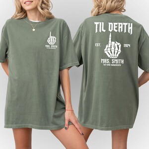 Może przedstawiać: Zielony T-shirt z białym szkieletowym palcem środkowym. Tekst "TIL DEATH" znajduje się nad palcem, a "MRS. SMITH" pod palcem. Tekst "EST. 2024" znajduje się po prawej stronie palca, a "VI-VIII-MMXXIV" pod palcem.