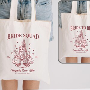 May include: Two white canvas tote bags with pink text and a pink outline of Cinderella's castle. The bag on the left says "Bride Squad" and the bag on the right says "Bride to Be". Both bags have the text "Happily Ever After" and the year 2024.