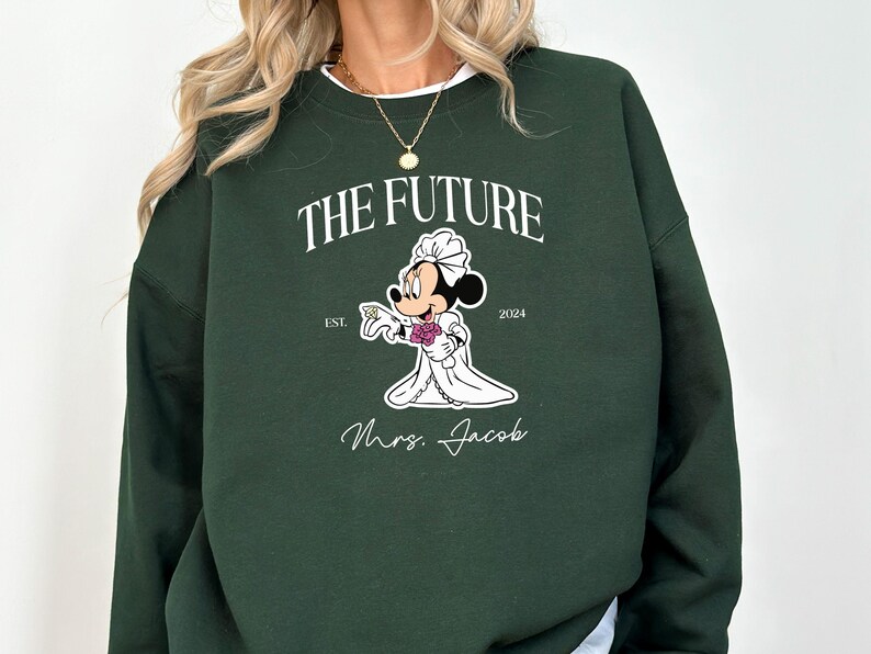 May include: A dark green sweatshirt with a white graphic of a cartoon mouse dressed as a bride. The text "The Future" is above the mouse and "Est. 2024" is below the mouse. The text "Mrs. Jacob" is below the mouse.