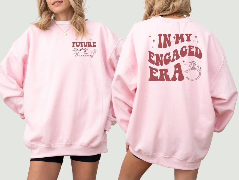 May include: Two pink sweatshirts with a red graphic print. One sweatshirt says "Future Mrs. Martinez" and the other says "In My Engaged Era" with a diamond ring graphic.