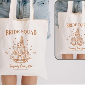 May include: Two white canvas tote bags with brown text and a line drawing of Cinderella's castle. The bag on the left says "Bride Squad" and the bag on the right says "Bride to Be". Both bags have the text "Happily Ever After" and the year "2024" printed on them.