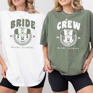 Puede incluir: Dos camisetas blancas con un gr&aacute;fico verde de Mickey Mouse. Una camiseta dice "Bride" y la otra dice "Crew". Ambas camisetas tienen el texto "2024 Miami, Florida".