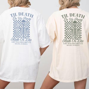 Może przedstawiać: Dwie duże koszulki, jedna biała i jedna kremowa, mają z tyłu grafikę szkieletu. Projekt zawiera frazy "TIL DEATH Do Us Party" i "Ride Or Die" z napisem "AMY BACHELORETTE MIAMI, FLORIDA" poniżej. Szkielet jest umieszczony na kratkowanym tle.