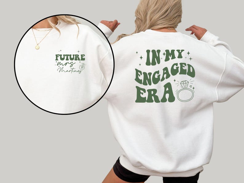 May include: White sweatshirt with green text that says "In My Engaged Era" with a diamond ring graphic. The back of the sweatshirt has green text that says "Future Mrs. Martinez" with a ring graphic.