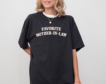 May include: Black t-shirt with the text "FAVORITE MOTHER-IN-LAW" in white, a white undershirt, and a gold necklace. The shirt is a casual style, suitable for everyday wear.