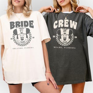 Puede incluir: Dos camisetas blancas con texto negro y una imagen de dibujos animados en blanco y negro de Minnie Mouse. El texto de la camiseta de la izquierda dice "Bride" y el texto de la camiseta de la derecha dice "Crew".