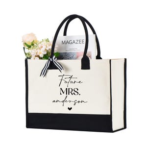 Op de afbeelding: Een witte canvas tote bag met zwarte bies en handvatten. De tas heeft de tekst "Future Mrs. Anderson" in het zwart op de voorkant gedrukt.