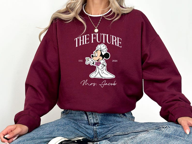 May include: Burgundy sweatshirt with a white graphic of Mickey Mouse dressed as a bride. The graphic says "The Future" with "Est. 2024" and "Mrs. Jacob" below the image.