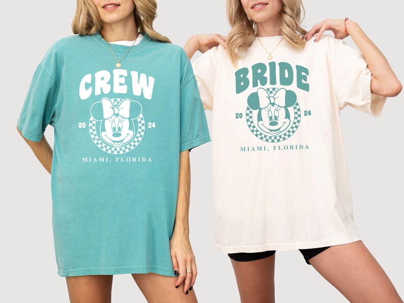 Puede incluir: Dos camisetas de gran tama&ntilde;o con un gr&aacute;fico de Mickey Mouse y texto. La camiseta azul claro dice "CREW" y la camiseta blanca dice "BRIDE". Ambas camisetas tienen el texto "Miami, Florida" y los n&uacute;meros "20" y "24" impresos en ellas.