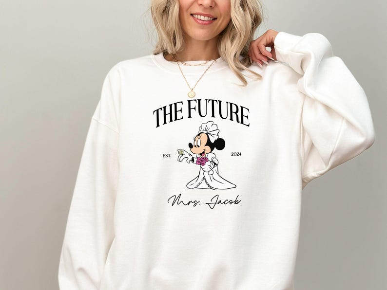 May include: White sweatshirt with a black graphic of a bride Mickey Mouse holding a ring. The text reads "The Future Est. 2024 Mrs. Jacob".