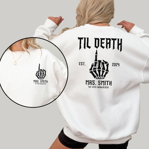 May include: White sweatshirt with black text that reads "TIL DEATH" and "MRS. SMITH" with a skeleton hand giving the middle finger. The text also includes the dates "EST. 2024" and "VI-VIII-MMXXIV".