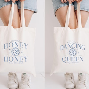 May include: Two white tote bags with blue text and a disco ball graphic. The left bag says "I found my honey" and "Honey" with the year 1972 and 2024. The right bag says "Chicago, IL Dancing Queen" with the year 1972 and 2024.