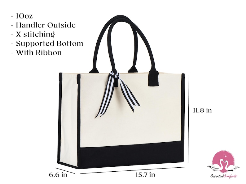 Op de afbeelding: Een witte canvas tote bag met zwarte bies en een zwarte bodem. De tas heeft een zwart lint dat om de handvatten is gebonden. De tas is 15,7 inch breed, 11,8 inch hoog en 6,6 inch diep.