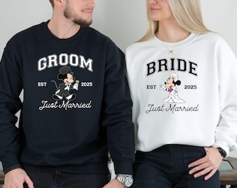 May include: A couple's matching black and white sweatshirts with Mickey Mouse and Minnie Mouse graphics. The groom's sweatshirt says "Groom Est 2025 Just Married" and the bride's sweatshirt says "Bride Est 2025 Just Married".