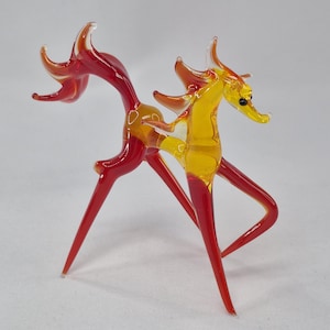 Può includere: Statuetta in vetro di una creatura mitica, con coda e zampe rosse, e corpo e testa gialli. La statuetta ha un design sottile con dettagli appuntiti.