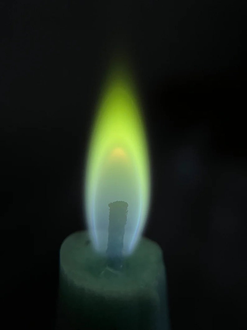 May include: A green candle with a yellow and blue flame burning.