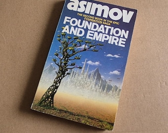 Może przedstawiać: Książka w miękkiej oprawie w stylu vintage zatytułowana "Foundation and Empire" autorstwa Asimova. Okładka przedstawia drzewo, futurystyczne miasto i błękitne niebo. Książka jest drugą z epickiej sagi Foundation.