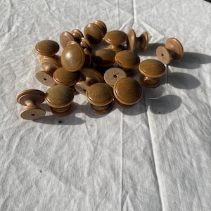 Könnte beinhalten: Eine Sammlung von 17 braunen Holzknöpfen mit leicht erhöhtem Rand und einem kleinen Loch in der Mitte. Die Knöpfe liegen auf einer weißen Oberfläche.