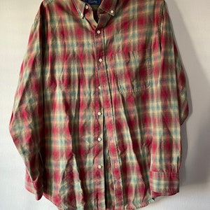 Puede incluir: Una camisa de manga larga a cuadros rojos, verdes y tostados con el nombre de la marca "Rainforest Country" en la etiqueta.