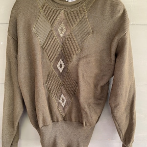 May include: A green sweater with a diamond-shaped pattern and brown leather accents. The sweater has a crew neck and long sleeves. The brand name "Semplce" is visible on the tag.