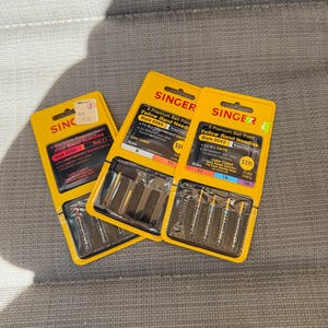 May include: Three packages of Singer sewing machine needles. One package contains 4 Premium Regular Point Red Band Needles style 2020 for lightweight woven fabrics. Two packages contain 4 and 5 Premium Ball Point Yellow Band Needles style 2045 for knits.